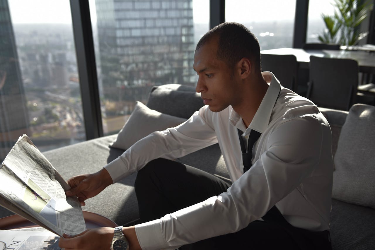 Young professional reading a newspaper in an urban office with cityscape view.